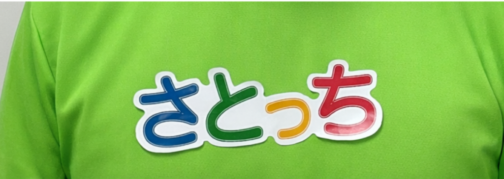 緑のtシャツに手作りの名札「さとっち」